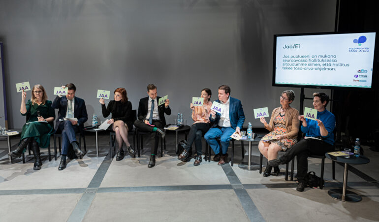 Kuva vaalipaneelista, jossa paneeliin osallistujat pitävät JAA-kylttiä ilmassa.